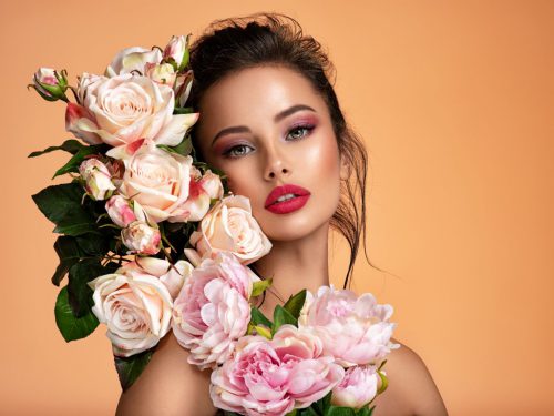 Attractive brunette girl with big beautiful bouquet of flowers. Beautiful white girl with flowers. Pretty woman with bright makeup. Art portrait with flowers.